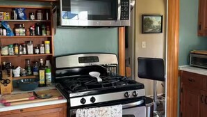 A kitchen with a stove, oven, microwave, and wooden cabinets. - Experience Classic Charm in a Cozy 115-Year-Old Colonial (Waltham)