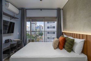 Ein Hotelzimmer mit Bett, Schreibtisch mit Stuhl, Fernseher und Balkon mit Stadtblick.