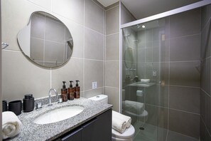 A modern bathroom with a granite sink, a round mirror, a glass-enclosed shower, and a toilet. - Nik Perdizes (São Paulo)