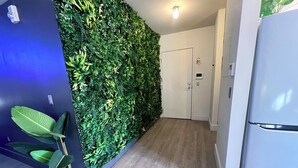 Ein Flur mit grüner, mit Pflanzen bewachsener Wand, einer weißen Tür und einem weißen Kühlschrank.