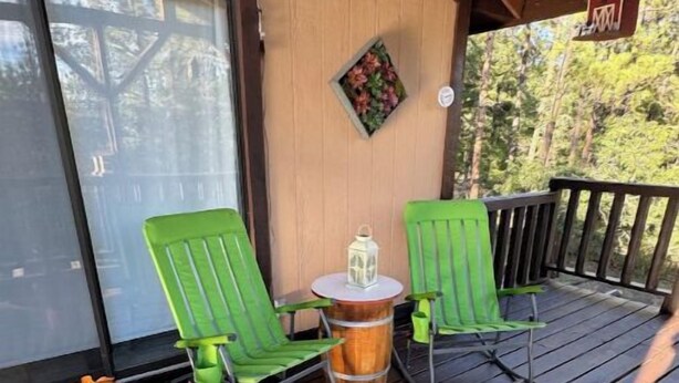 Eine Holzterrasse mit zwei grünen Stühlen, einem kleinen Tisch, einer Laterne und einem Wanddekor.