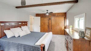 Un dormitorio con una cama grande, cabecera de madera, ventilador de techo, cómoda con cajones y una ventana que proporciona luz natural.