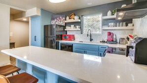 A modern kitchen with a large island, blue cabinets, and various appliances including a refrigerator, microwave, and coffee maker. - Modern Mtn-View Designer Home in Medicine Park (Medicine Park)