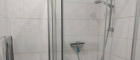 A glass-enclosed shower stall with a handheld showerhead and a wall-mounted faucet.