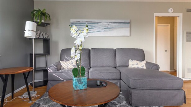 A modern living room with a grey sectional sofa, a round wooden coffee table, and a floor lamp. - Large 1BR Retreat, Steps from Shops & Market (Pasadena)