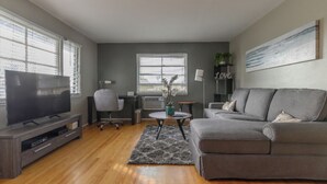 A modern living room with a grey sofa, a flat-screen TV, a coffee table, and a grey rug. - Large 1BR Retreat, Steps from Shops & Market (Pasadena)