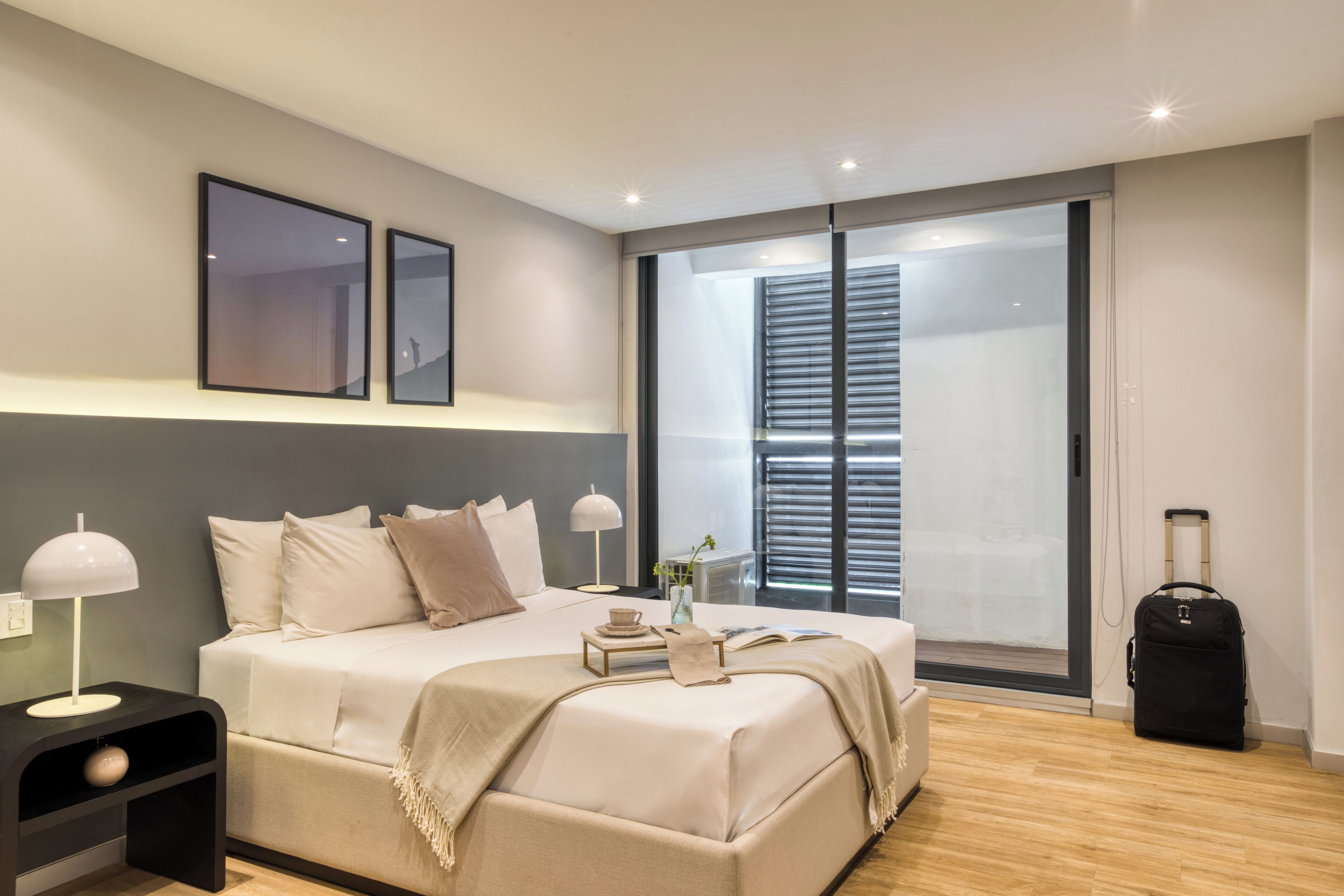 A modern hotel room with a large bed, bedside lamps, a suitcase, and a view of the outside through a large window.