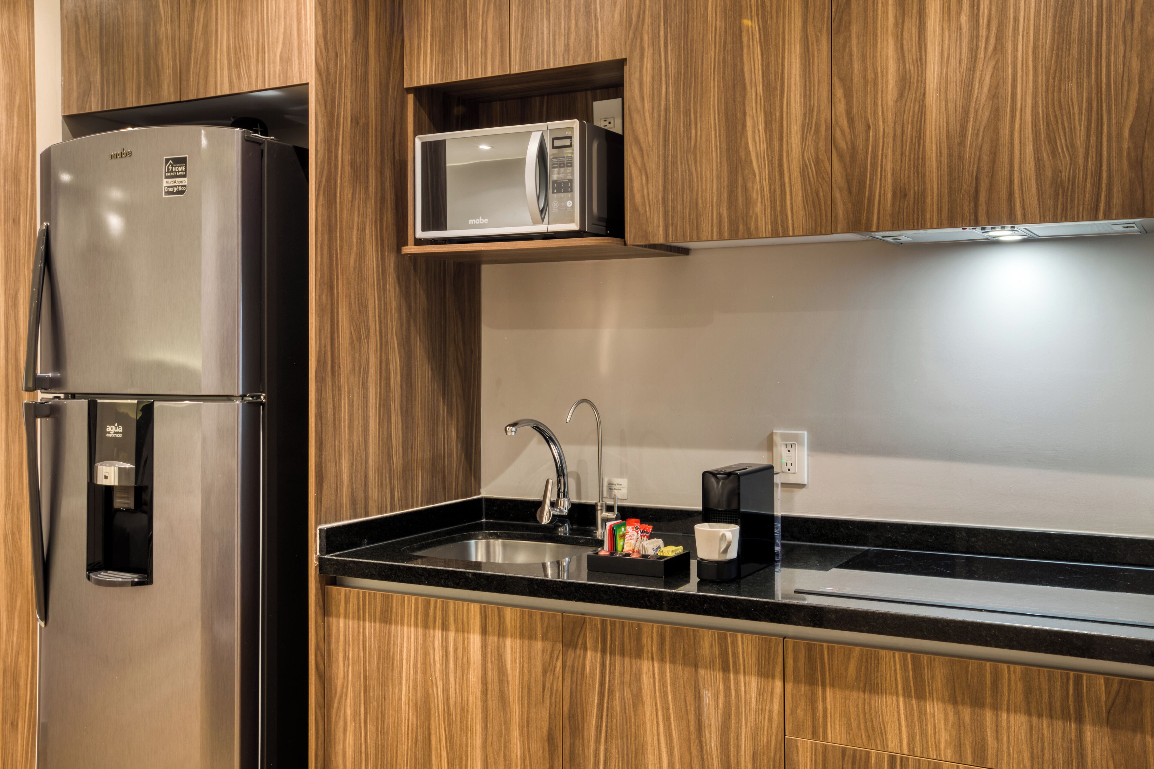 Una cocina moderna con un refrigerador de acero inoxidable, un microondas y un lavamanos empotrado.