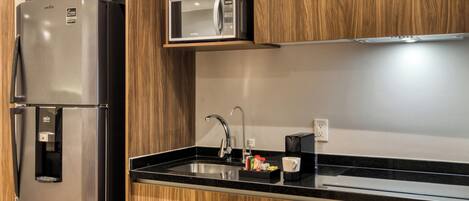Una cocina moderna con un refrigerador de acero inoxidable, un microondas y un lavamanos empotrado.