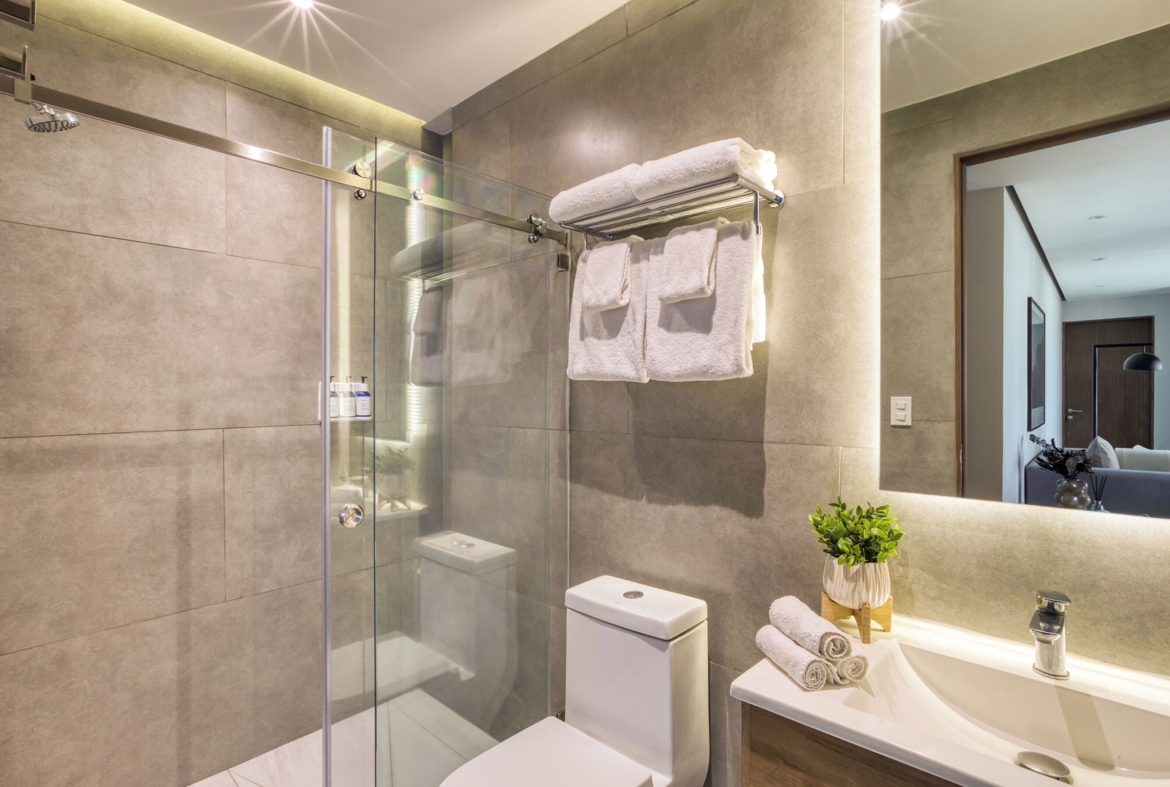 A modern bathroom with a glass-enclosed shower, a toilet, and a sink with a mirror.
