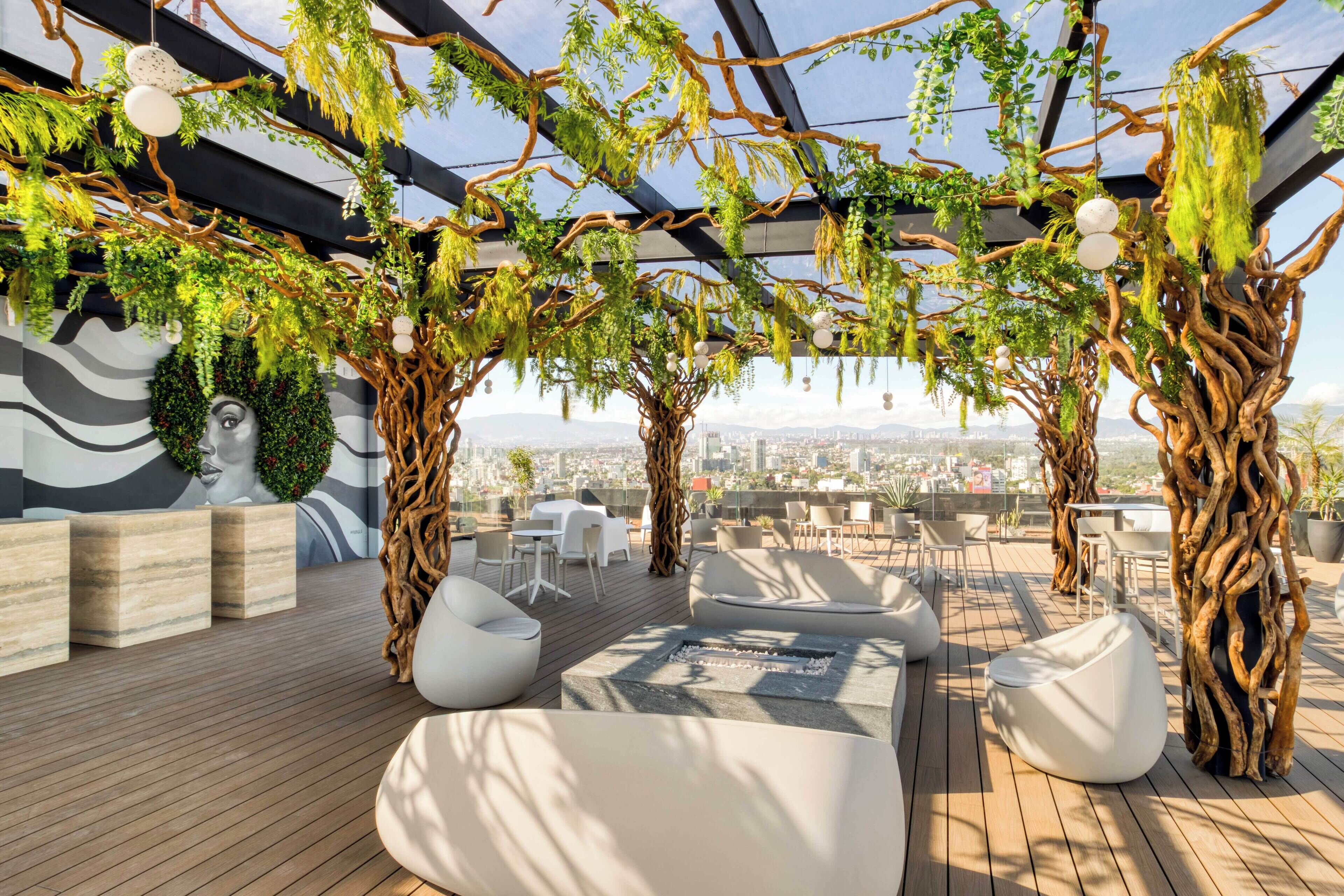 A rooftop lounge with wooden flooring, white seating, and a view of the cityscape.