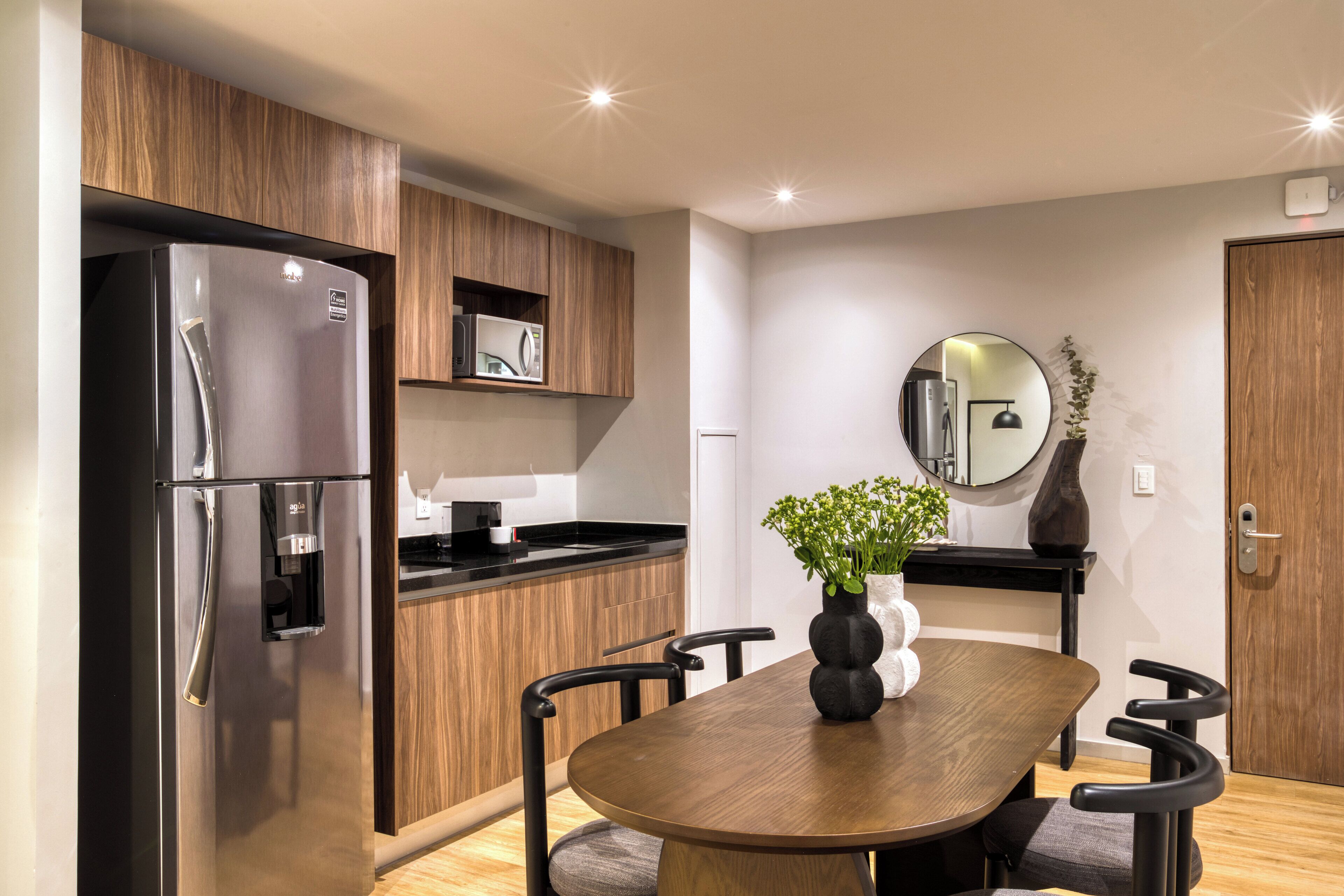 Una cocina moderna con un refrigerador de acero inoxidable, armarios de madera, una encimera negra y una mesa de comedor con sillas.