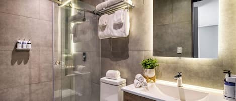 Un baño moderno con ducha de vidrio, inodoro, lavamanos con espejo y toallas dobladas en un escurreplatos.