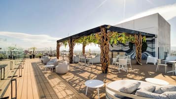 A rooftop terrace with modern seating, a pergola with greenery, and a city view.