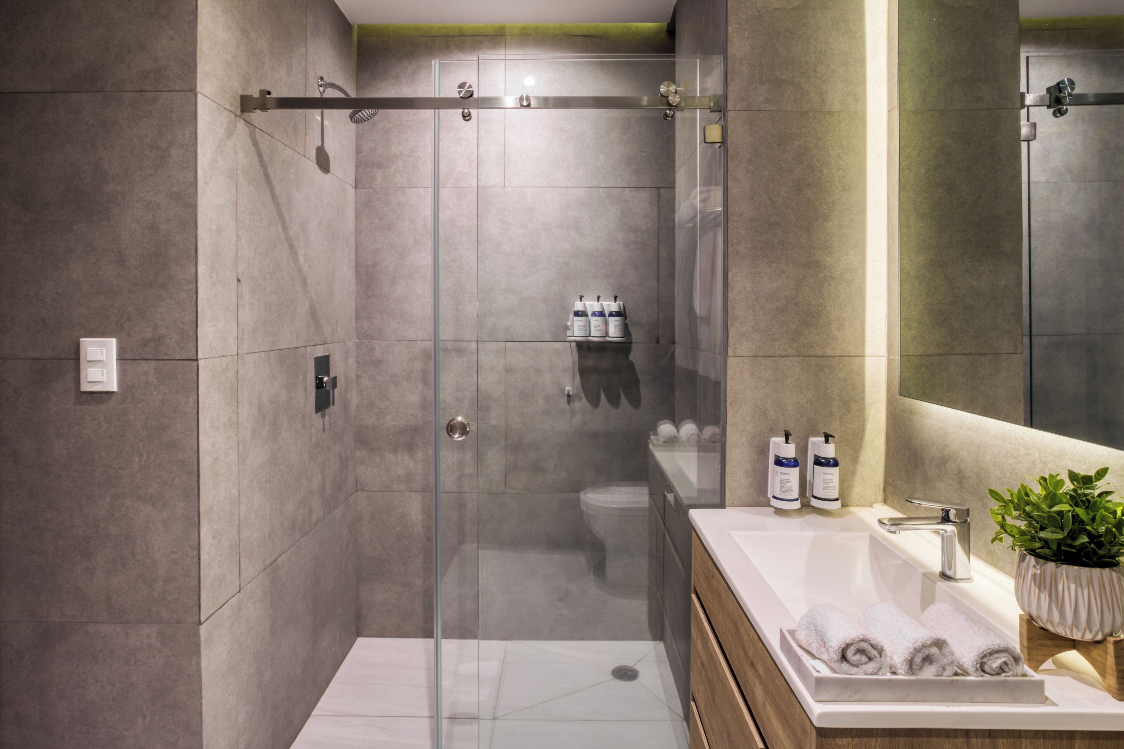 A modern bathroom with a glass-enclosed shower, a white sink with a wooden vanity, and a mirror above the sink.