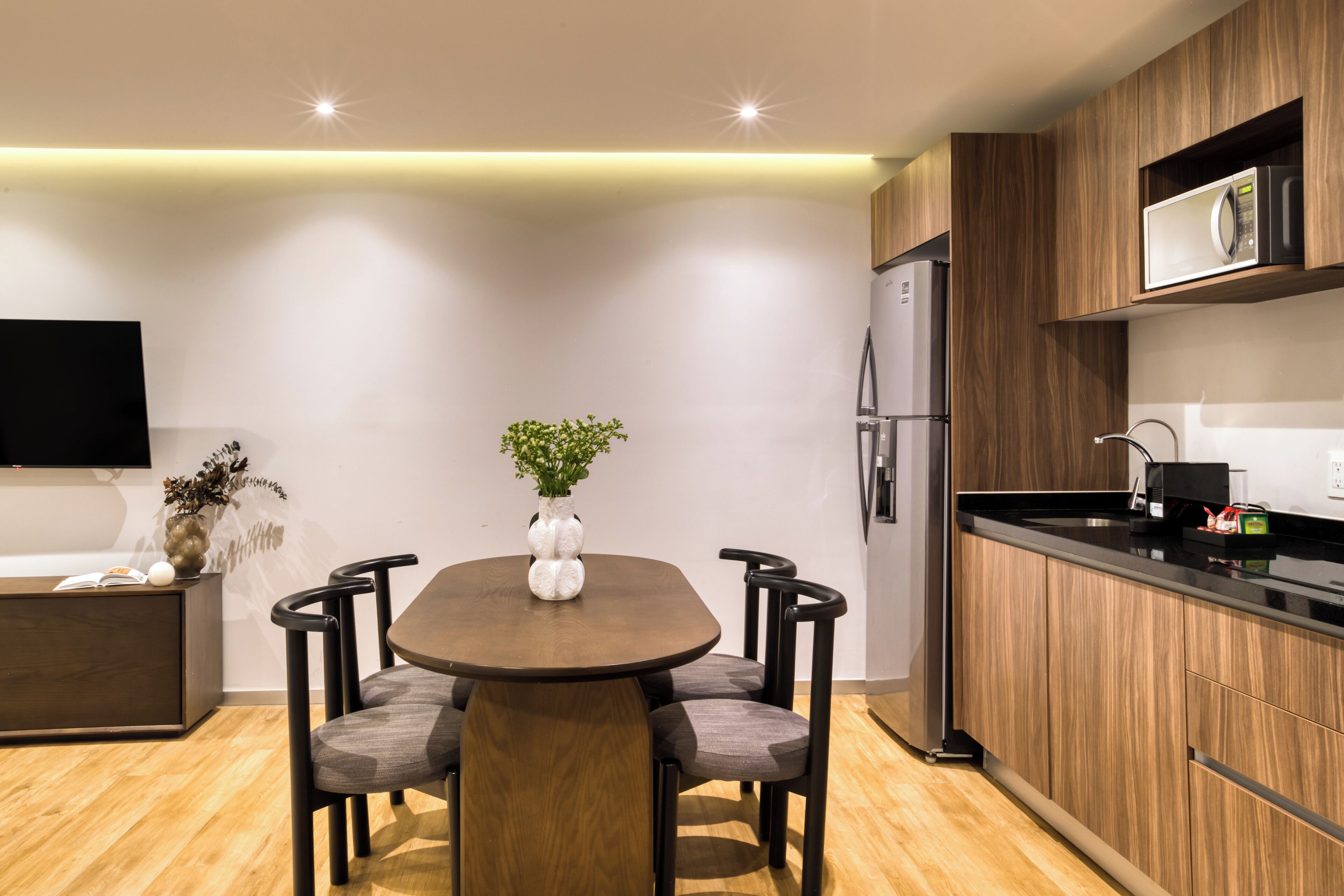 Una cocina moderna con armarios de madera, microondas integrado y un comedor con mesa y sillas de madera.