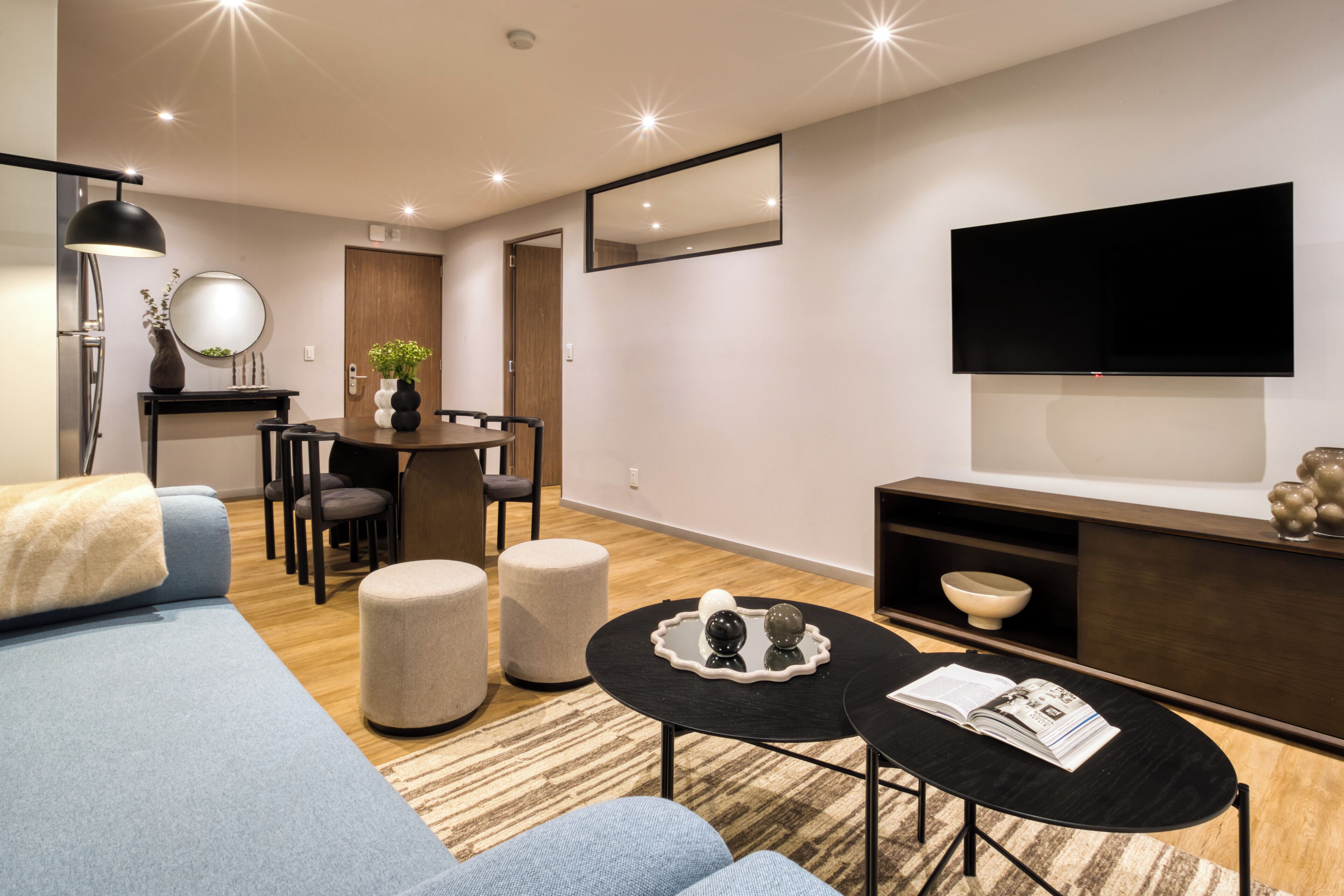 A modern living room with a sofa, ottomans, a coffee table, a dining area with chairs, a TV, and a fireplace.