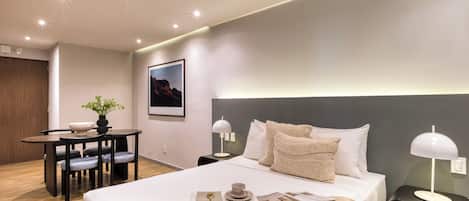 Una habitación de hotel moderna con una cama grande, mesitas de noche con lámparas, un escritorio pequeño con una silla y una planta en maceta.