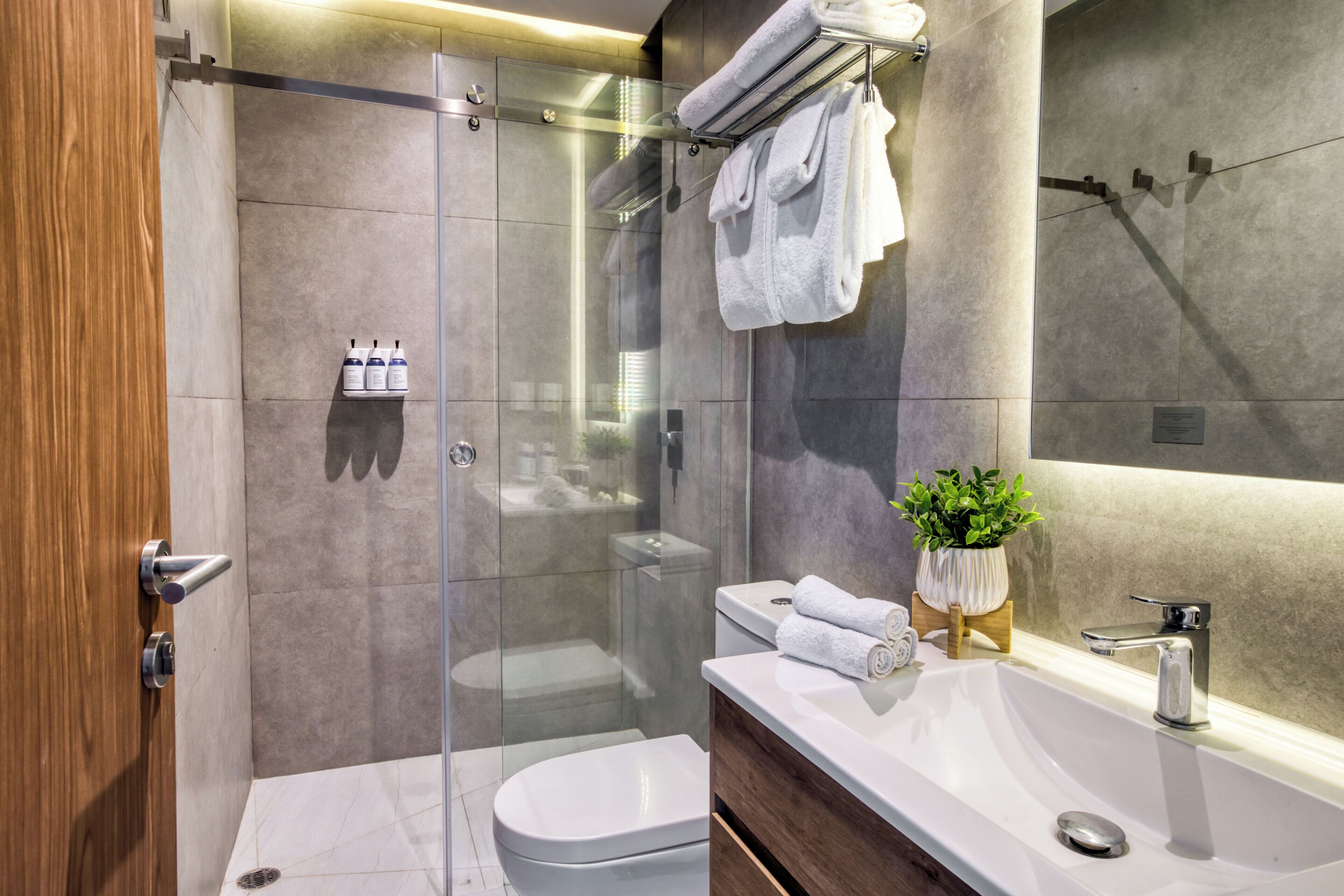Un baño moderno con ducha de vidrio, inodoro blanco y tocador con lavamanos y espejo.