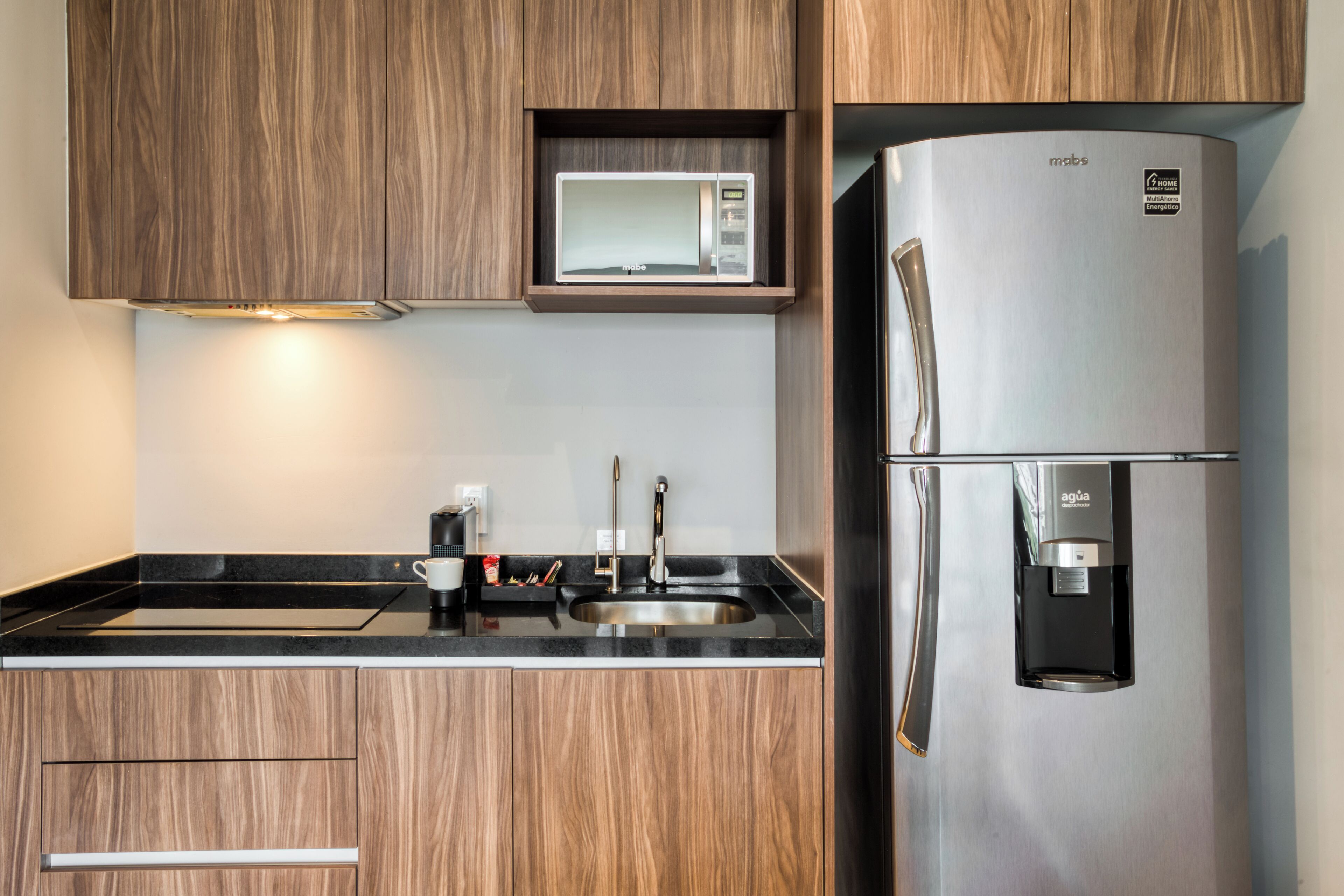 A modern kitchen with wooden cabinets, a stainless steel refrigerator, a built-in microwave, and a water dispenser.
