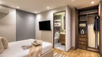 Een moderne slaapkamer met een bed, nachtkastje, televisie en een inloopkast met spiegel en hangende kleding.