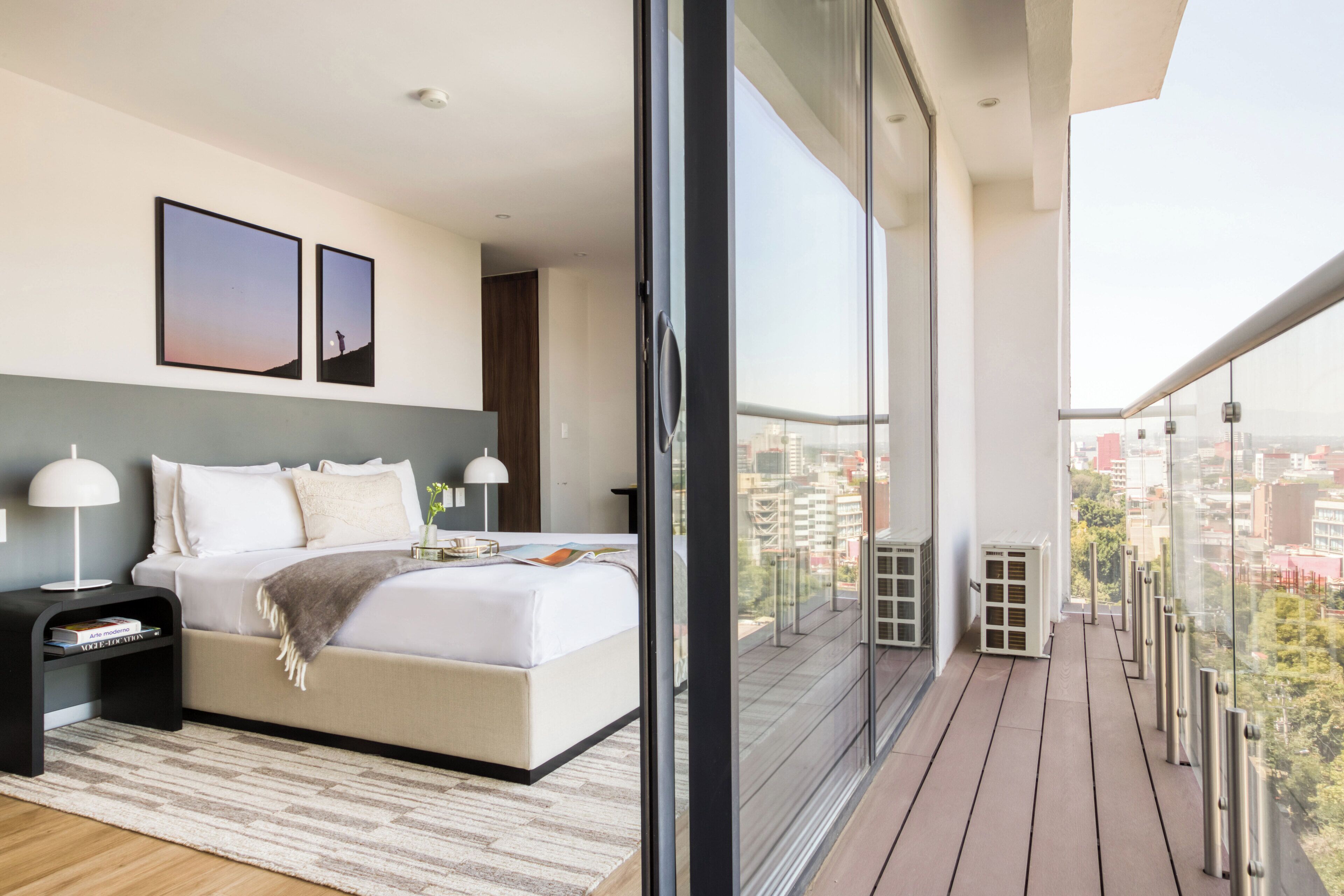 A modern bedroom with a large bed, bedside tables, and a view of the city through floor-to-ceiling windows.
