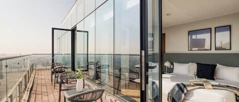 A modern hotel room with a balcony, a bed, and a view of the city.