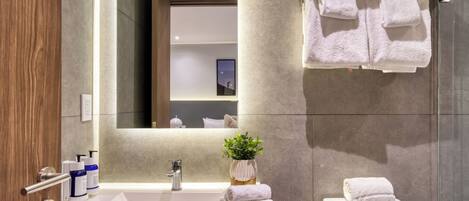 A modern bathroom with a large sink, a mirror, and a toilet. There are towels hanging on a rack and a potted plant on the sink.