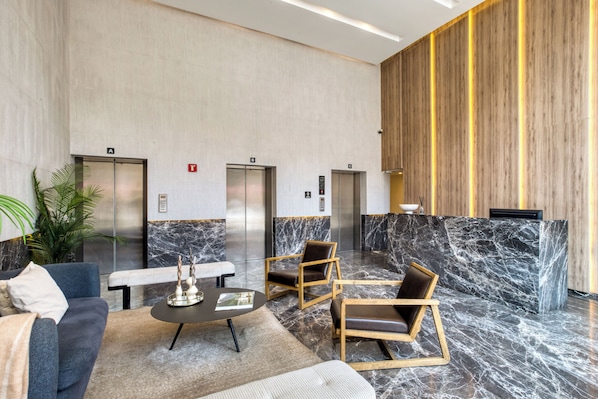 Una hall con una reception in marmo, due ascensori, un divano, un tavolino da caffè e una pianta in vaso.