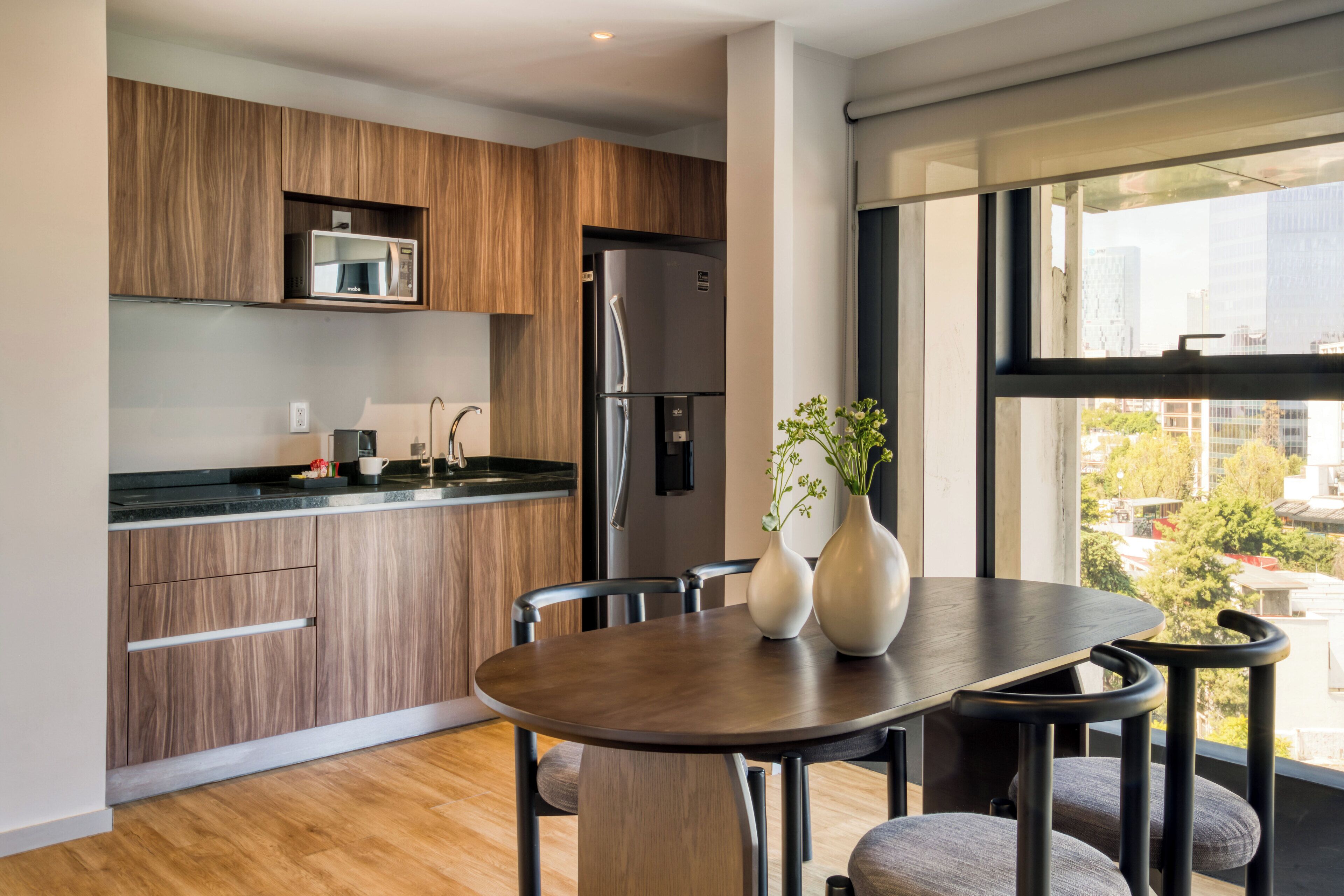 A modern kitchen with wooden cabinets, a stainless steel refrigerator, and a dining area with a round table and chairs.