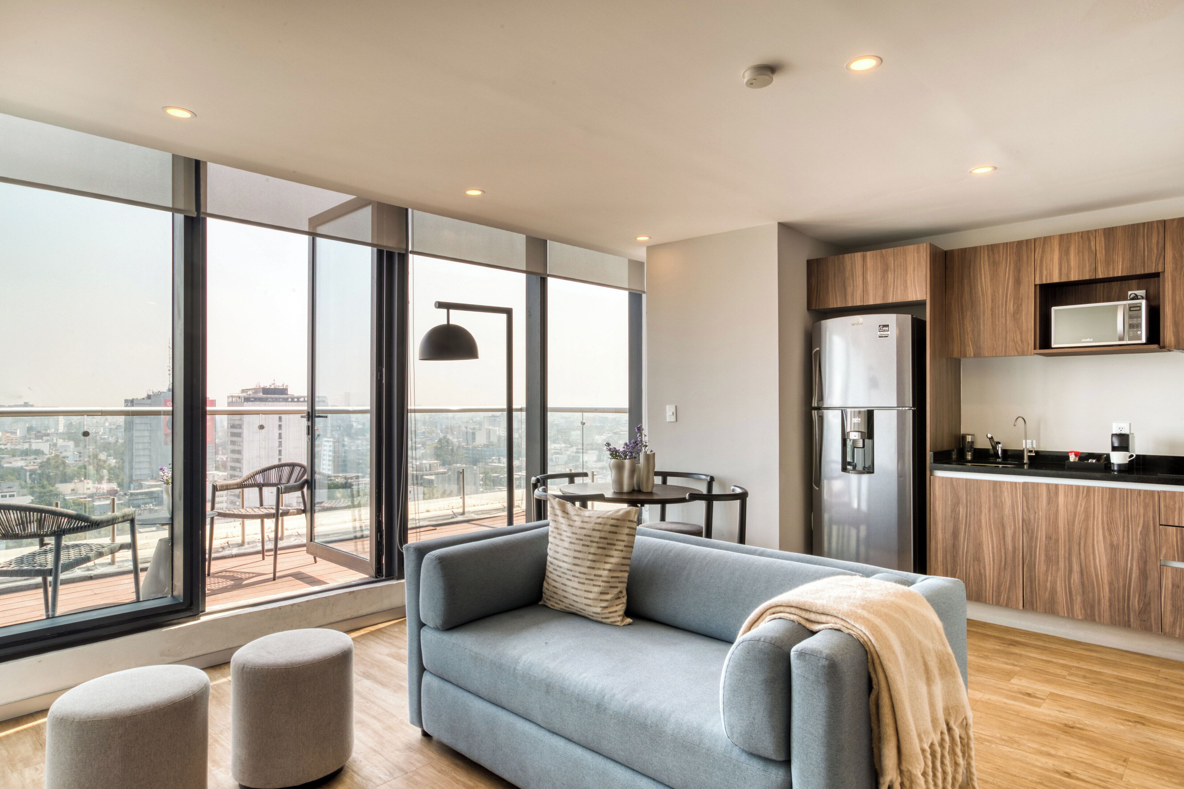 En moderne lejlighed med balkon, sofa, skottomanner, spisebord og et køkkenområde.