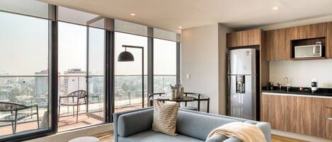 A modern apartment with a balcony, a sofa, ottomans, a dining table, and a kitchen area.