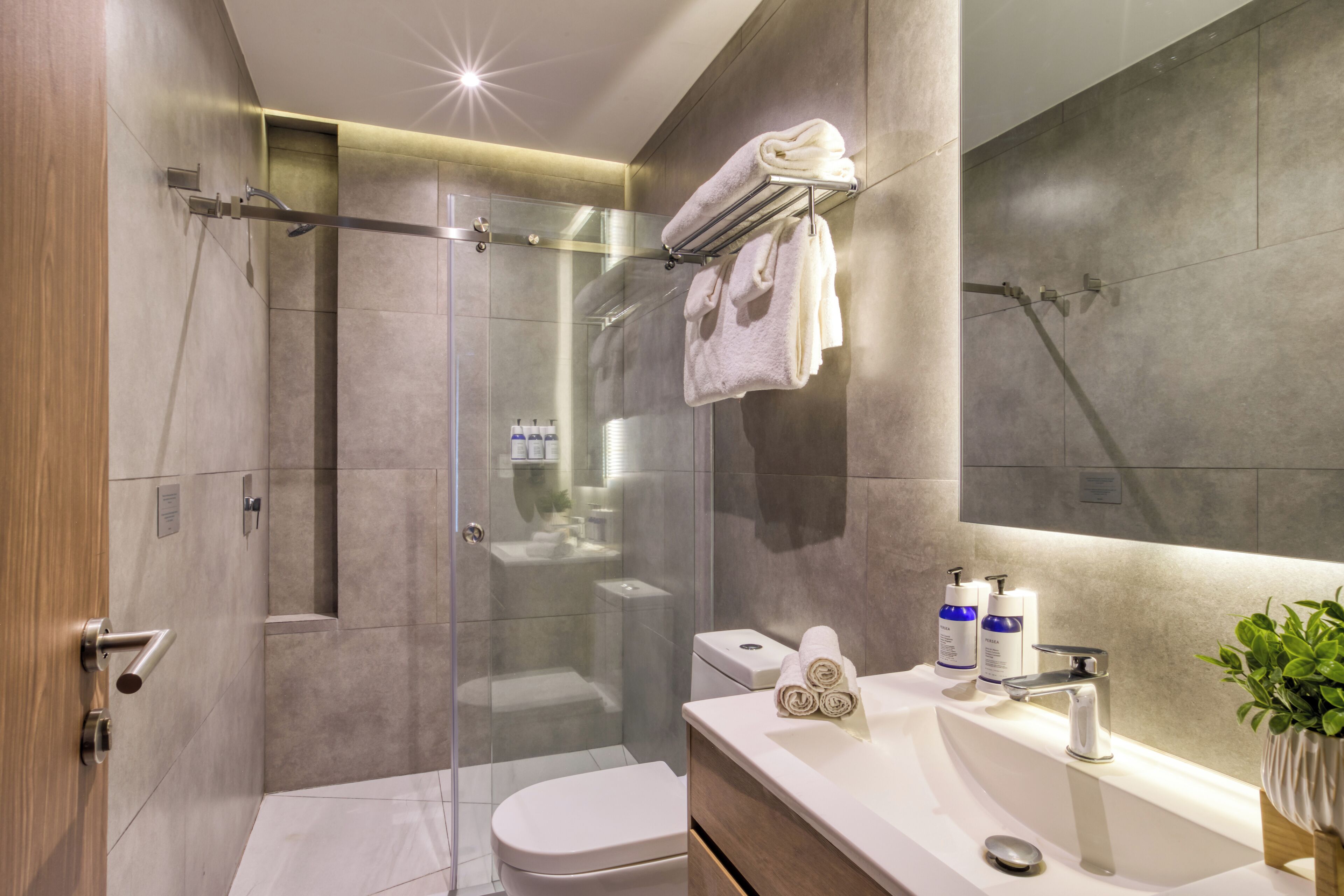 A modern bathroom with a glass-enclosed shower, a toilet, a sink with toiletries, and a mirror.