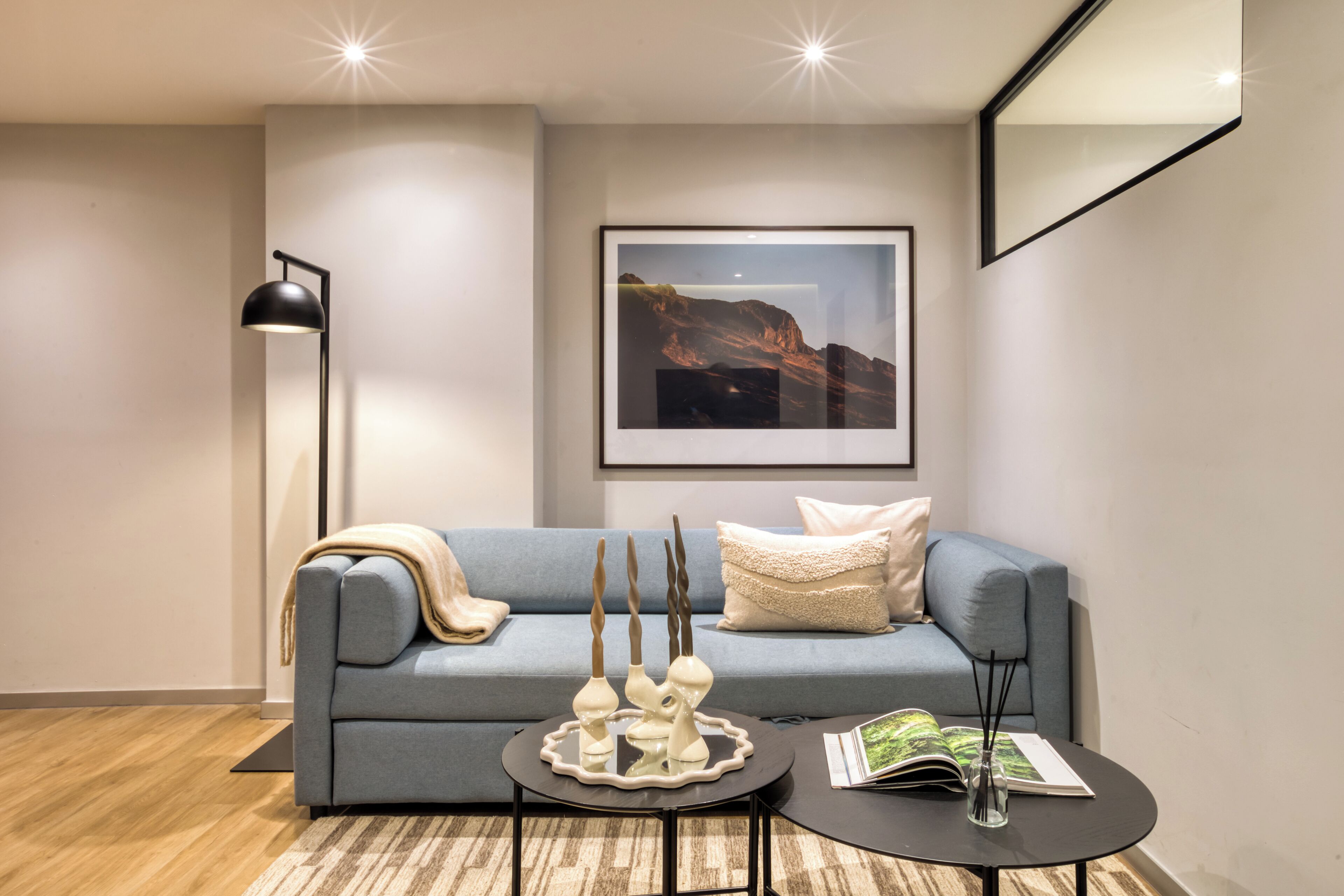 Een moderne woonkamer met een grijze bank, een ronde salontafel en een vloerlamp.