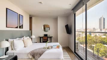 A modern hotel room with a large bed, a desk, a round mirror, and a TV on a wall.