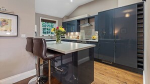 A modern kitchen with dark cabinets, a central island, and a window with blinds. - No. 1 - Laurel Cottage - Pass the Keys (York)