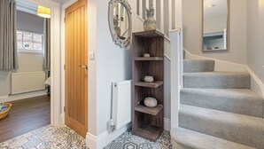 Un corridoio con una porta in legno, un termosifone, un tappeto a motivi decorativi, una scala rivestita di moquette grigia e uno specchio appeso al muro.