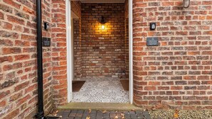 A brick building entrance with a tiled floor and a lit wall fixture. - No. 6 - Wisteria Cottage - Pass the Keys (Middlethorpe)