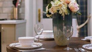 A dining table set with white plates, bowls, and wine glasses, accompanied by a vase of flowers. - No. 6 - Wisteria Cottage - Pass the Keys (Middlethorpe)