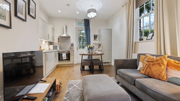 A modern living room with a grey sofa, a flat-screen TV, and a dining area with a table and chairs. - No. 6 - Wisteria Cottage - Pass the Keys (Middlethorpe)