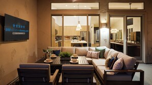 A modern living room with a sofa, chairs, a dining table, and a kitchen in the background.