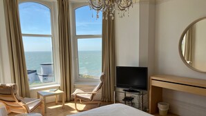 A hotel room with a bed, a TV, a desk, a chair, a small table, and a view of the ocean. - Bermuda House with parking, good sea view and minutes from beach and shops (Ventnor)