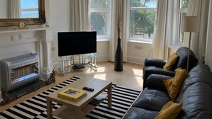 A living room with a TV, sofa, coffee table, fireplace, and large windows with curtains. - Bermuda House with parking, good sea view and minutes from beach and shops (Ventnor)