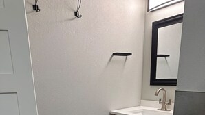Een badkamer met een witte deur, een houten wastafelmeubel, een spiegel en een toilet.