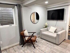 A living room with a sofa, a chair, a TV, and a mirror.