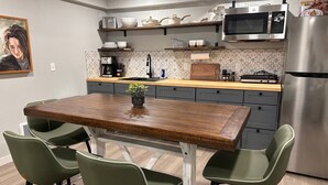 Een moderne keuken met een houten eettafel, groene stoelen en roestvrijstalen apparatuur.