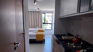 A hotel room with a bed, a small kitchenette, and a view of the outside. - Villas do Porto - 217 by La Playa (Ipojuca)