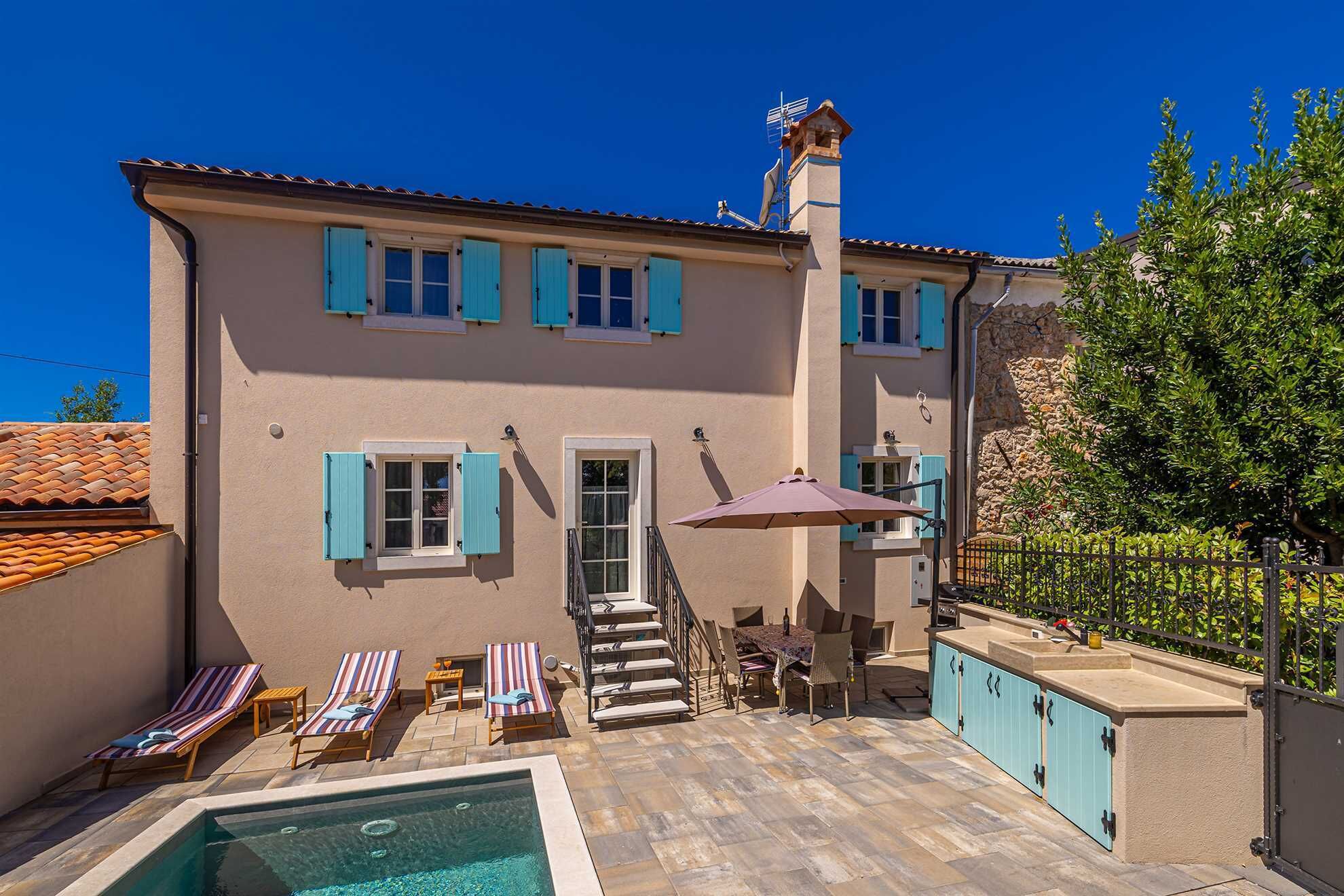 A two-story building with a swimming pool, outdoor seating, and a stone wall.