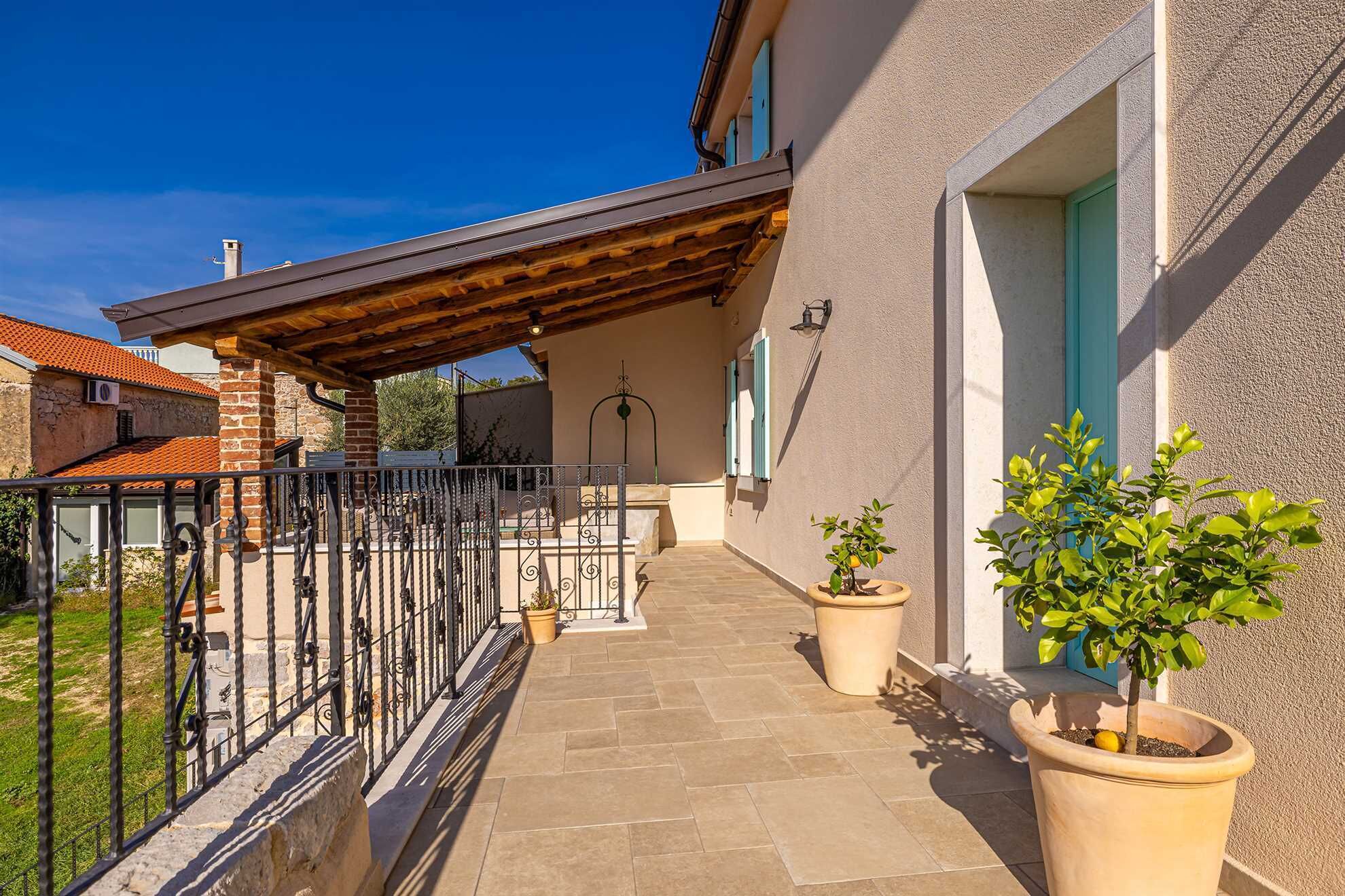 A covered outdoor area with a tiled floor, a metal railing, and potted plants.