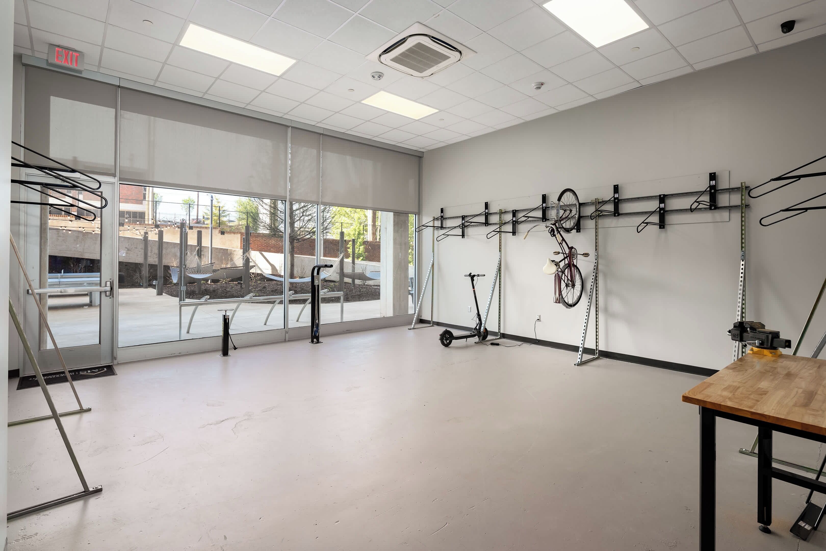 Una habitación amplia con ventanas grandes, una mesa de madera y varias bicicletas y scooters colgados en la pared.